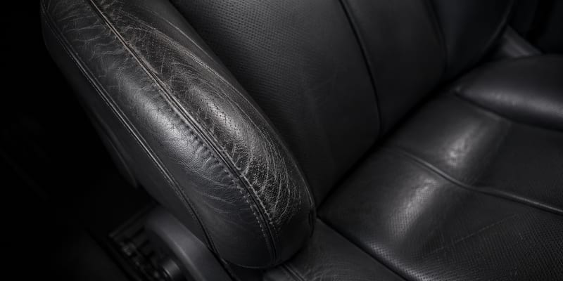 Macro of a worn leather seat bolster showing creasing and colour loss.